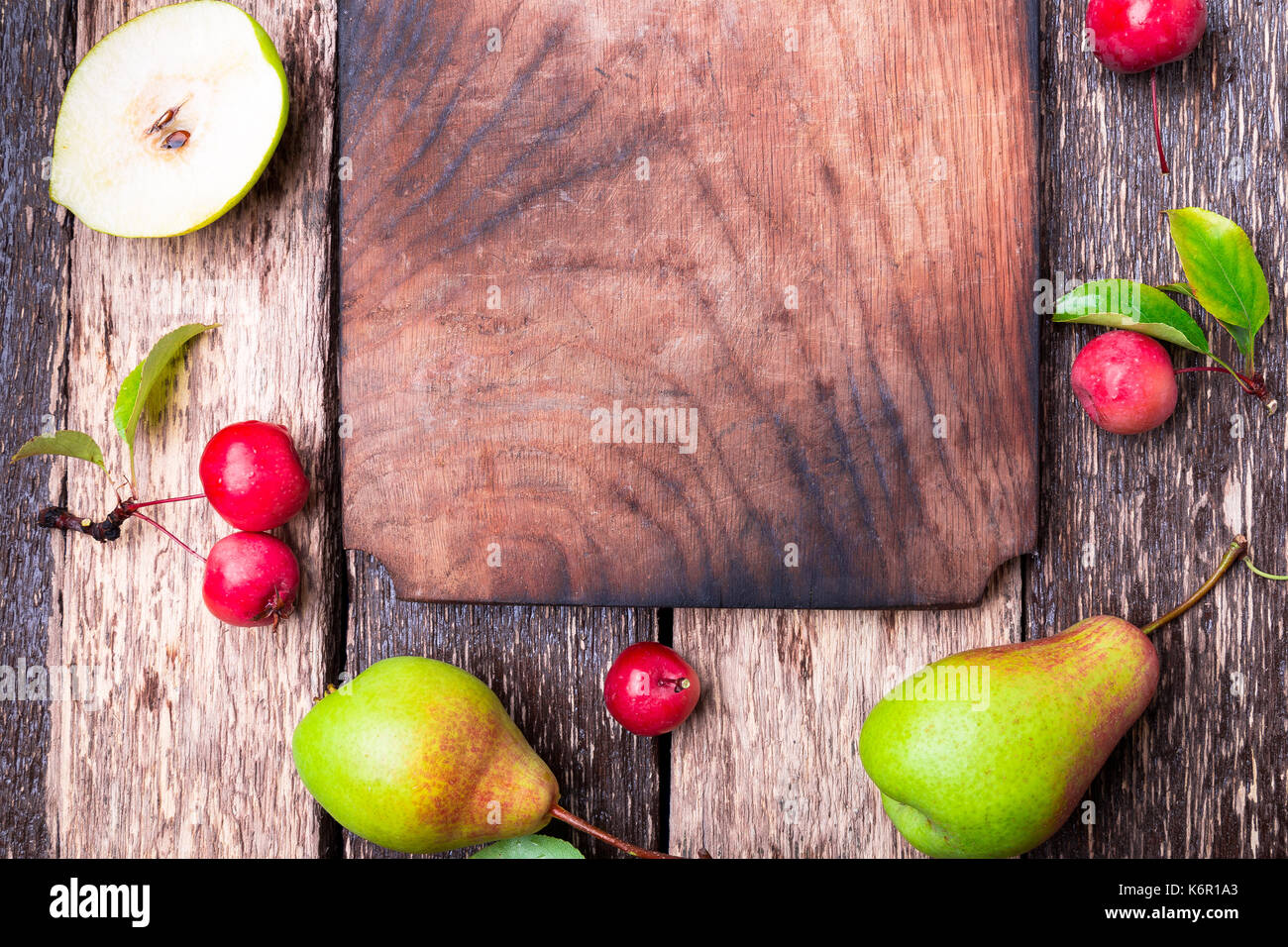 Pear and small apple around empty cutting board on wooden rustic background. Top view. Frame. Autumn harvest. Copy space Stock Photo