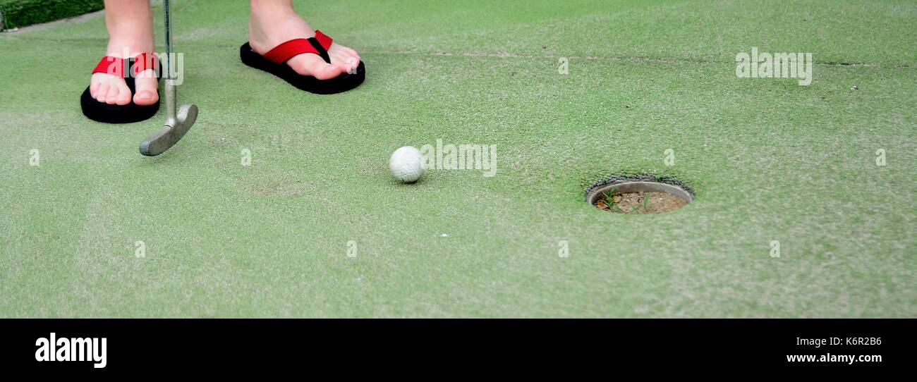 Playing mini golf. Low angle closeup view of mini golf ball and golf club near hole. Stock Photo