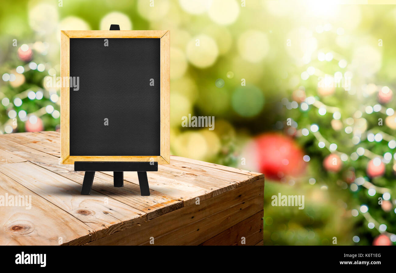 Blackboard with easel on wood table ( food stand ) at blur Christmas tree bokeh light background,Template mock up for display or montage of product or Stock Photo