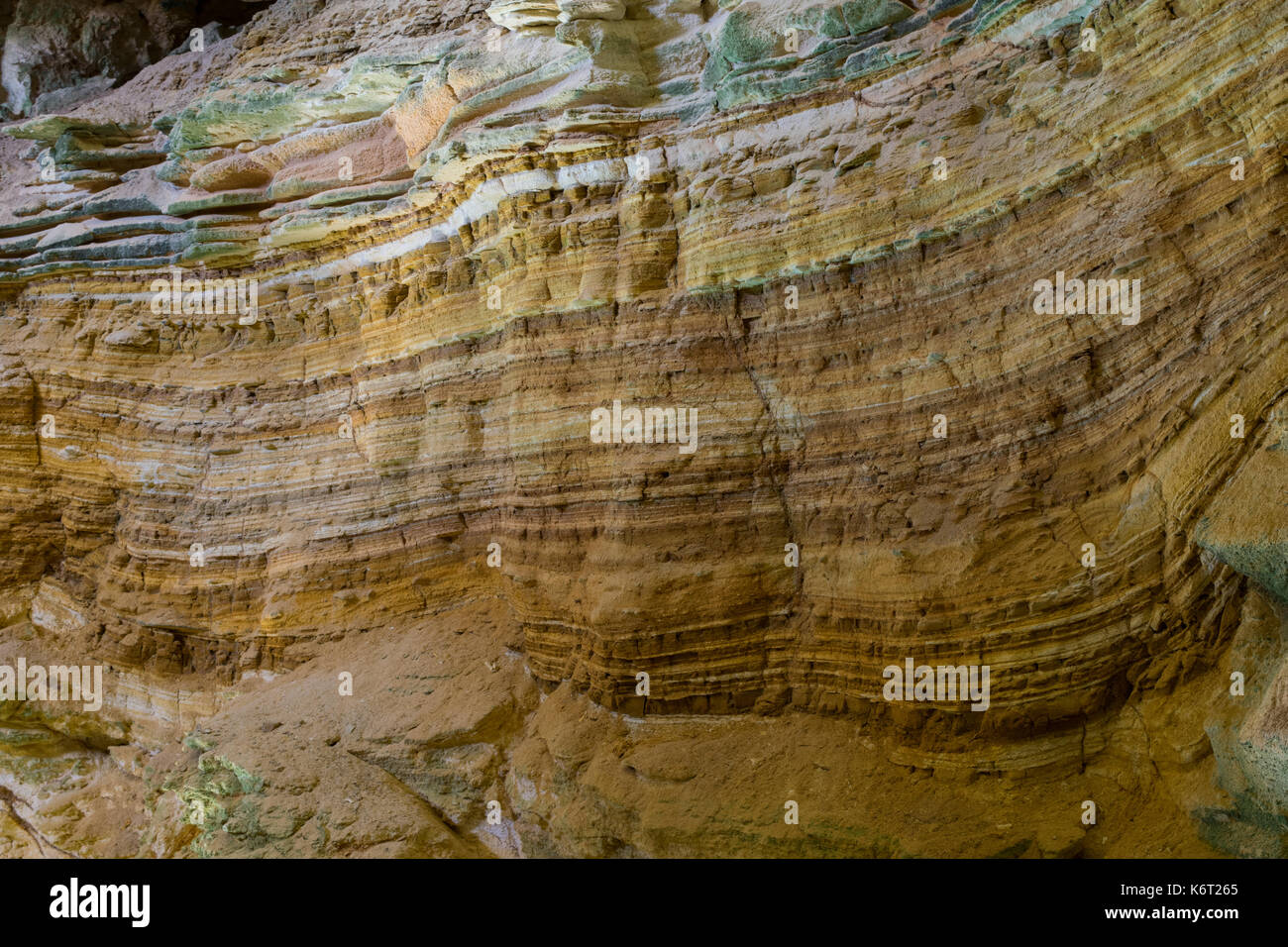 Cliff side cave, formed by sea erosion, containing evidence of sedimentation with different sediment layers having different colours. Cliffs in Malta Stock Photo