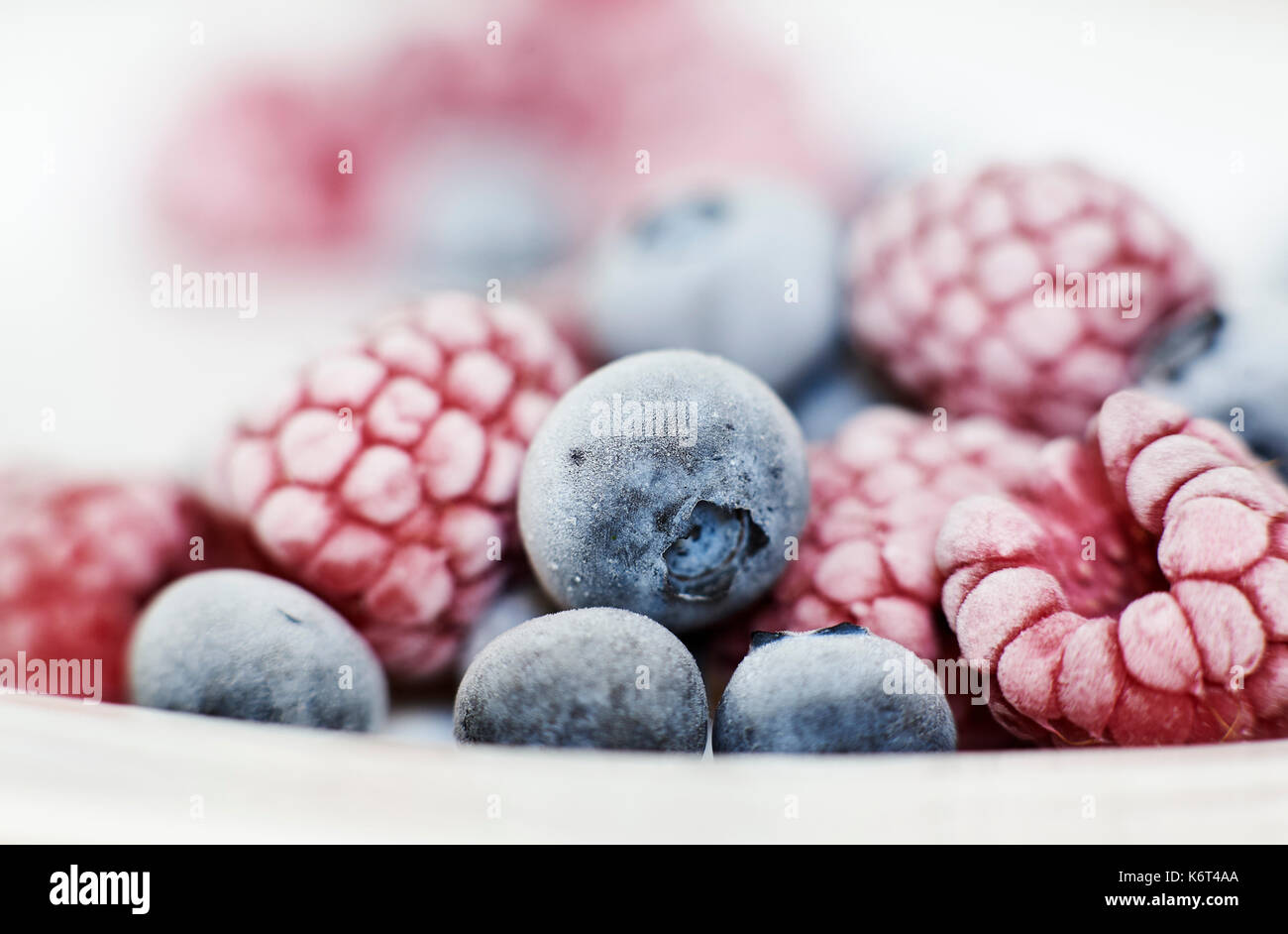 Close up of frozen blueberries and raspberries in a white bowl with frost on the skin of the high in Vitamin C super fruit for breakfast. Stock Photo