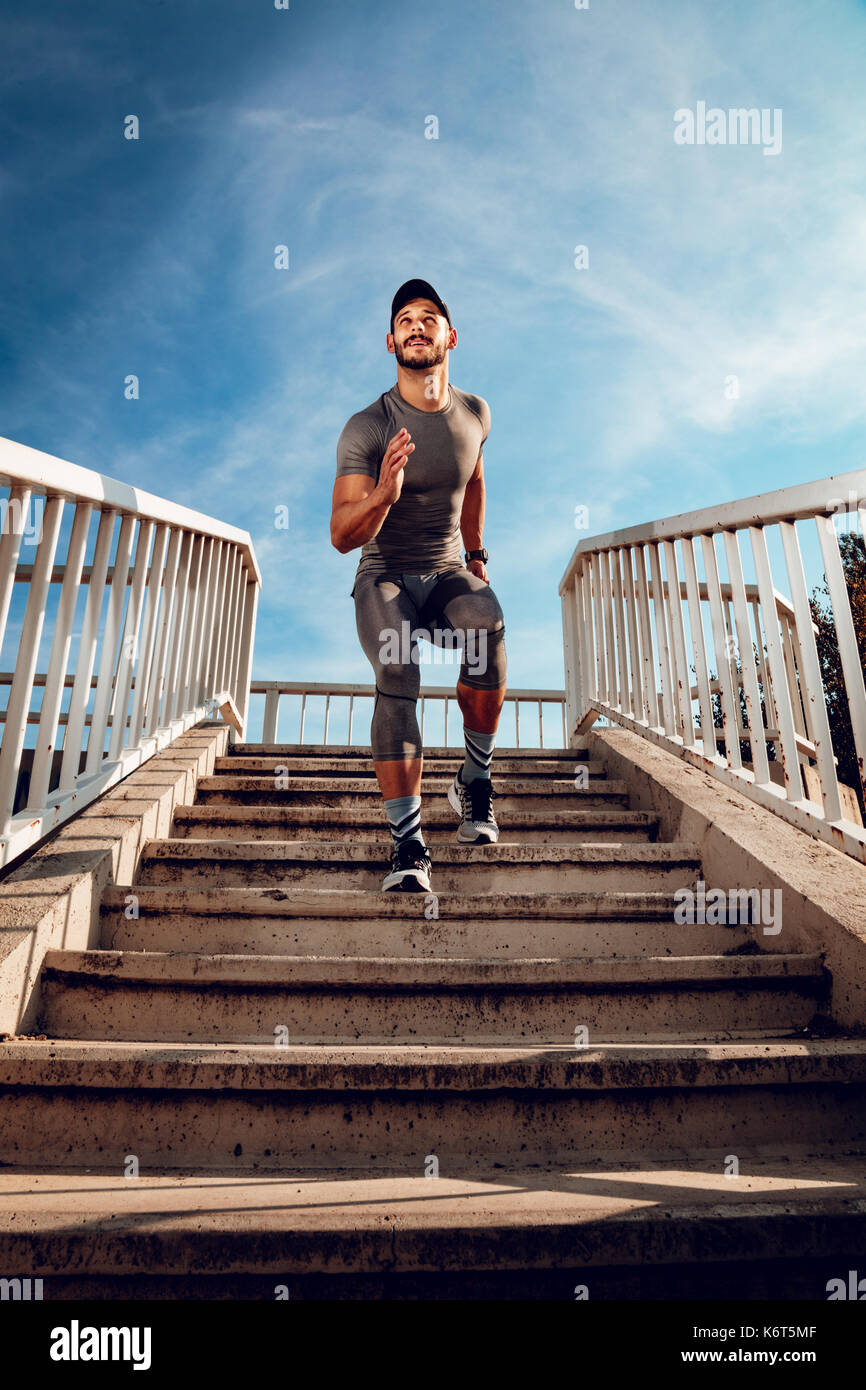 Young muscular sportsman running down the stairs at the bridge. Stock Photo