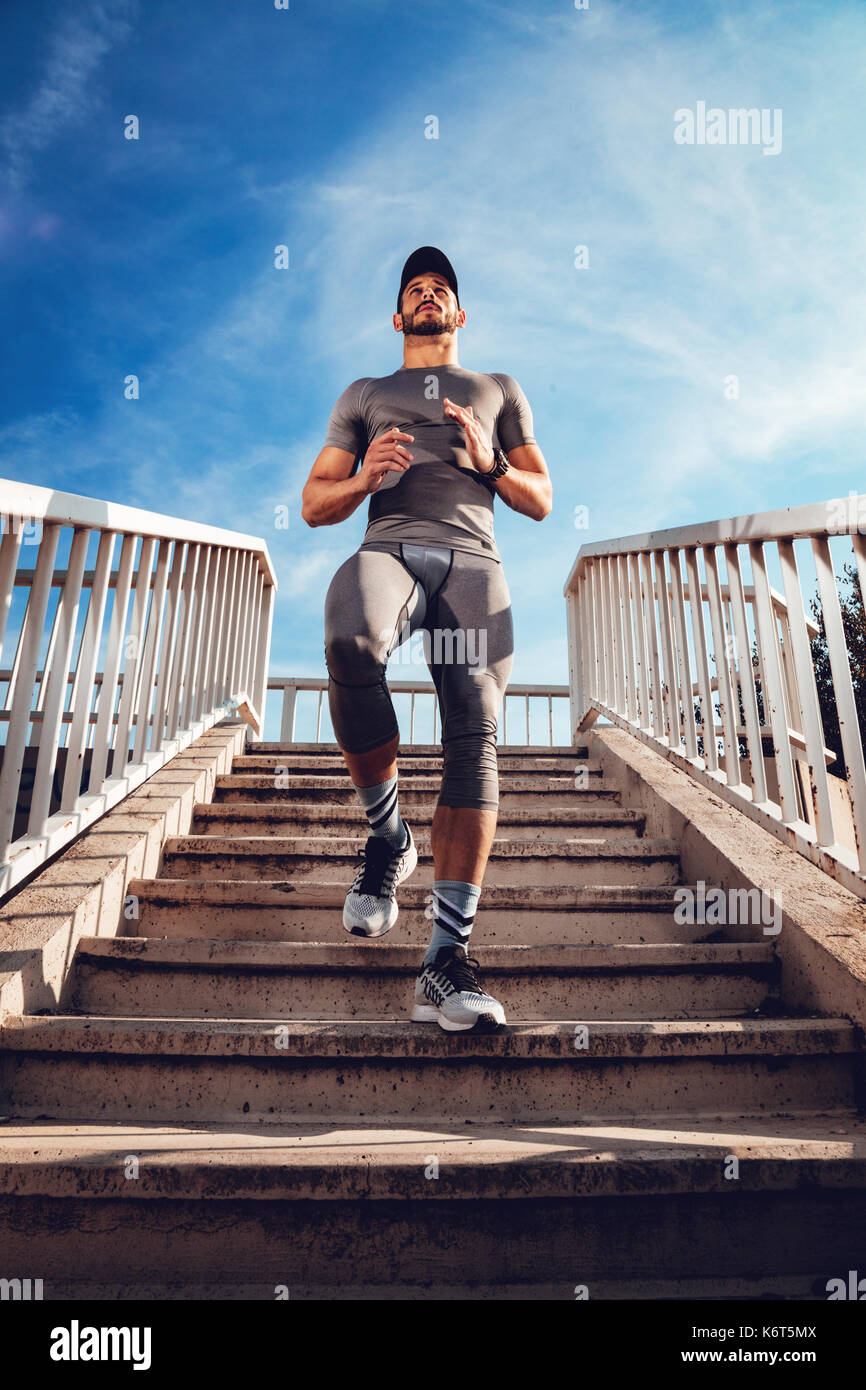 Young muscular sportsman jogging down the stairs at the bridge. Stock Photo