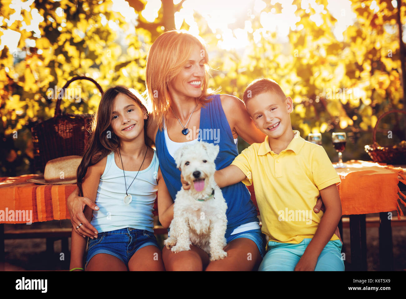 Beautiful smiling mother and her cute children with dog having picnic at a vineyard. Stock Photo