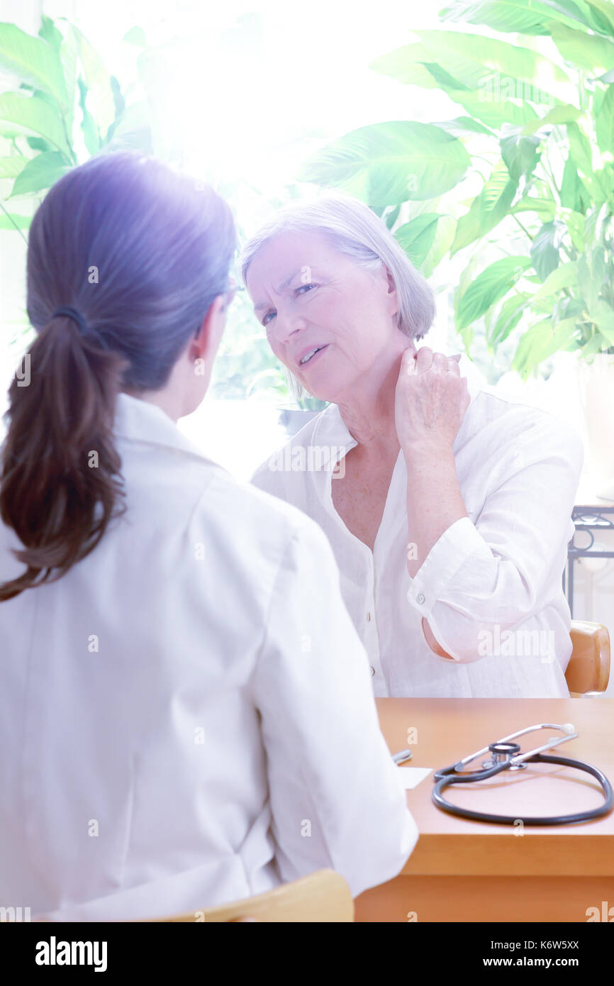 Senior female patient consulting her general practitioner or doctor on account of acute neck pain caused by muscular tension, copy space Stock Photo