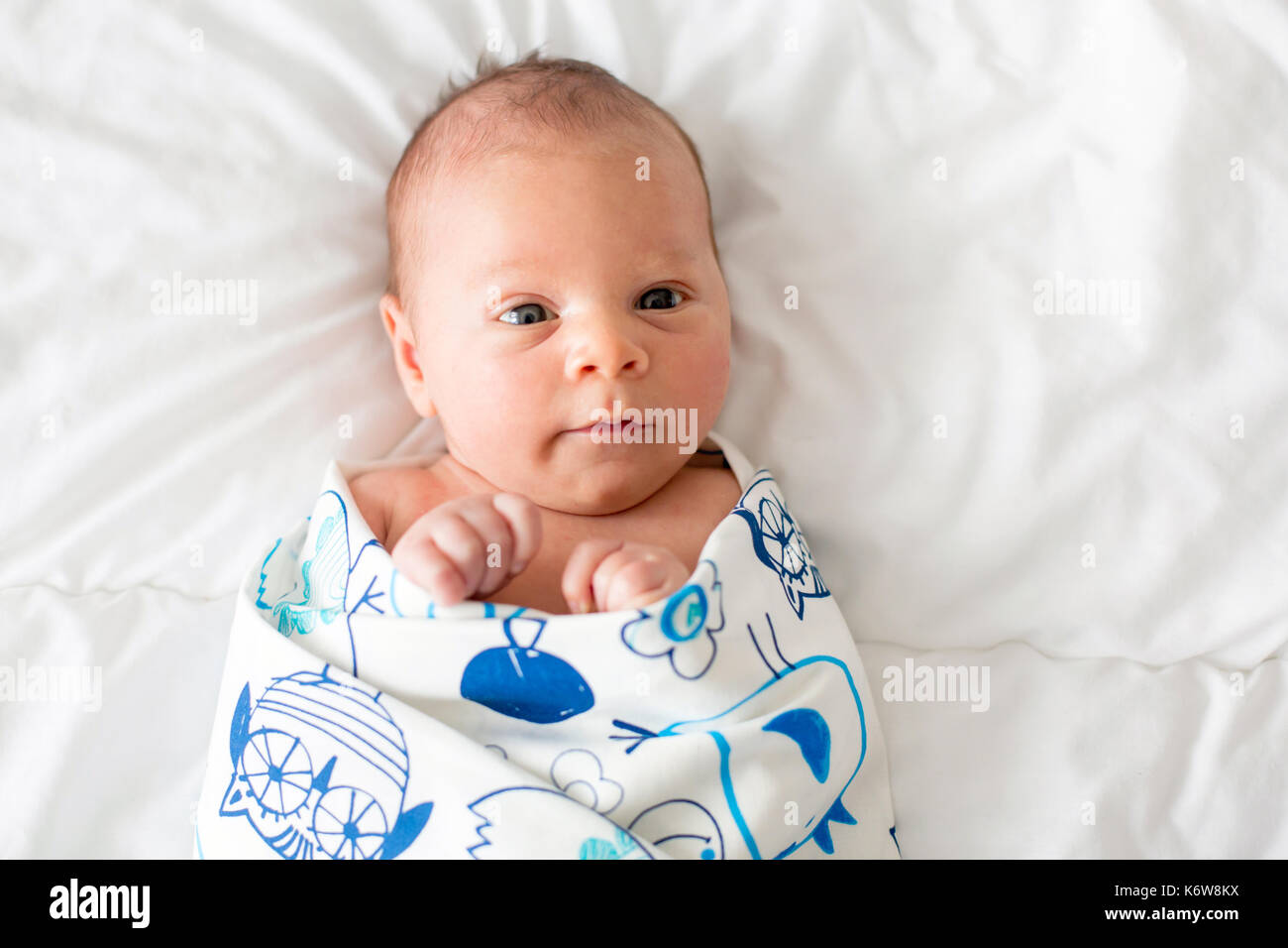 Cute newborn baby boy, lay in bed and looking curiously at camera at
