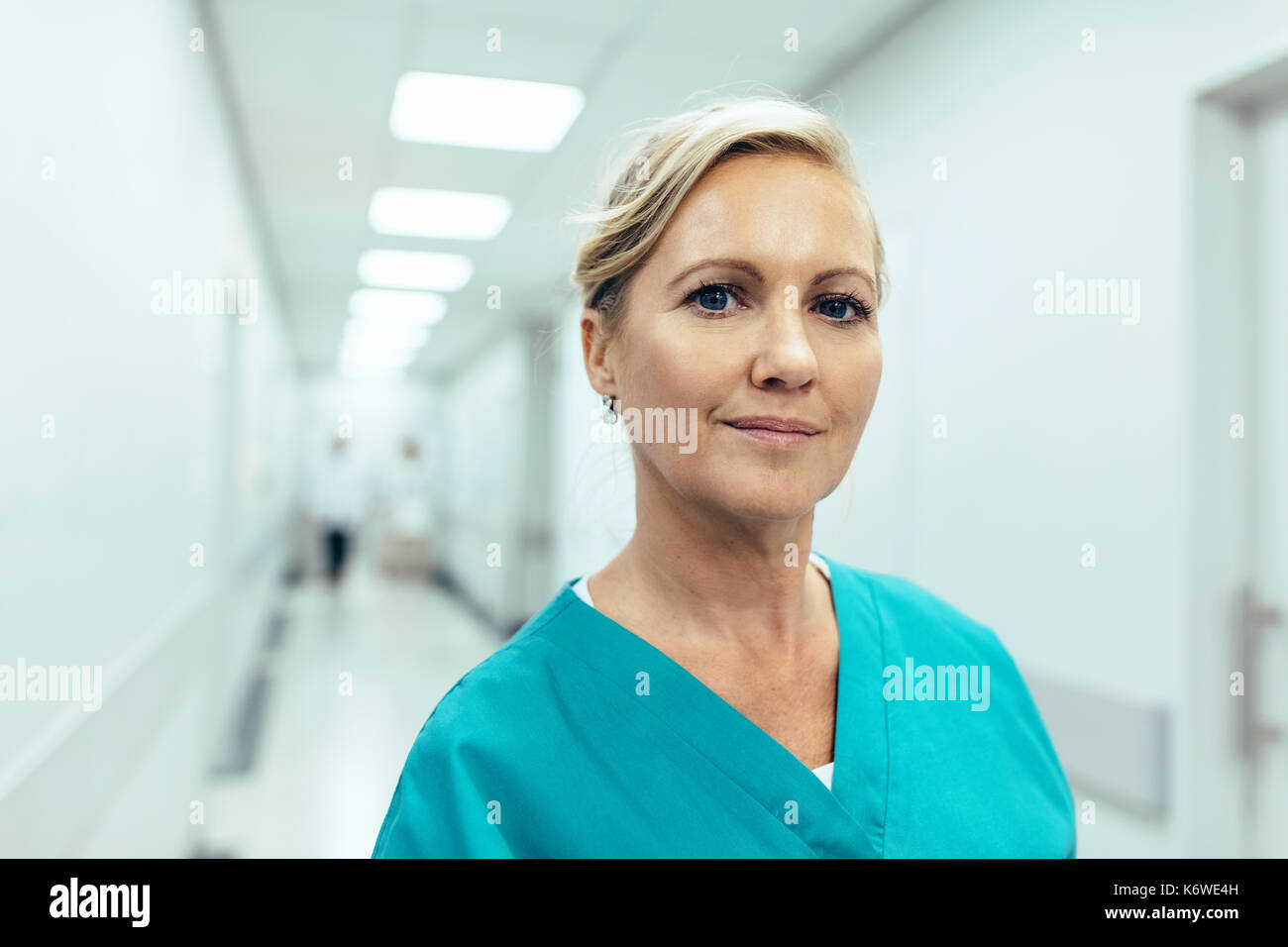 Close up portrait of female healthcare worker standing in hospital corridor. Caucasian woman in hospital hallway staring at camera. Stock Photo