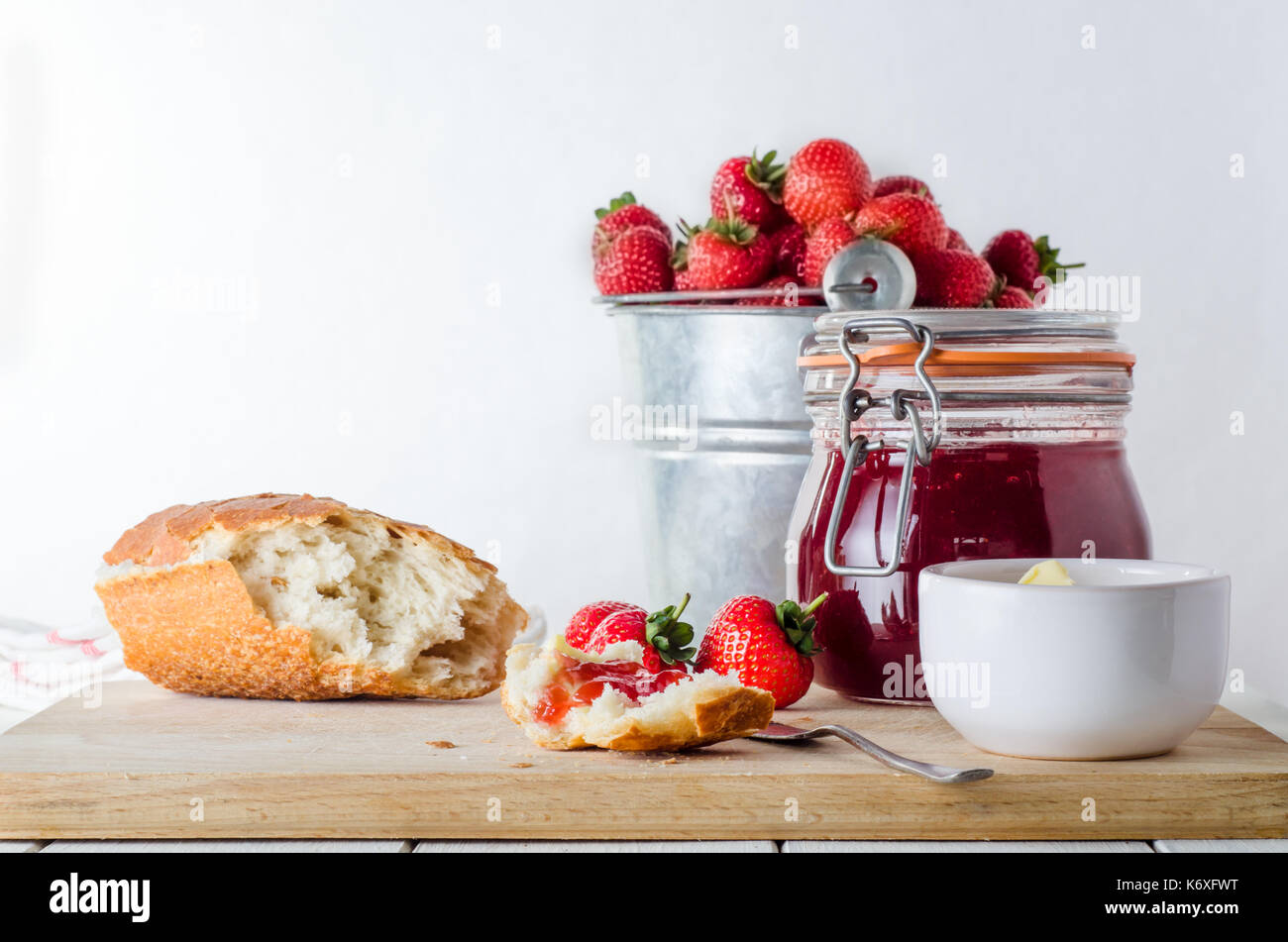 A kitchen table scene of freshly made strawberry jam in storage jar