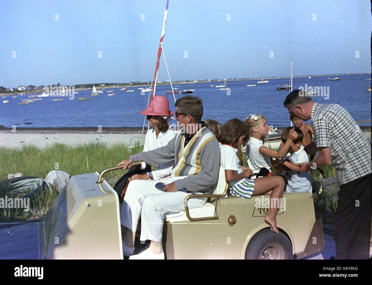 31 August 1963 President John F. Kennedy riding in a golf car after a cruise on the on the Honey Fitz  in Hyannisport, MA, August 31, 1963.  Also pictured are Jacqueline Kennedy, Maria Shriver, Sydney Lawford, Tim Shriver, and John F. Kennedy, Jr.  A secret service man is helping John Jr. to get onto the golf cart. Photograph by Cecil Stoughton. Stock Photo