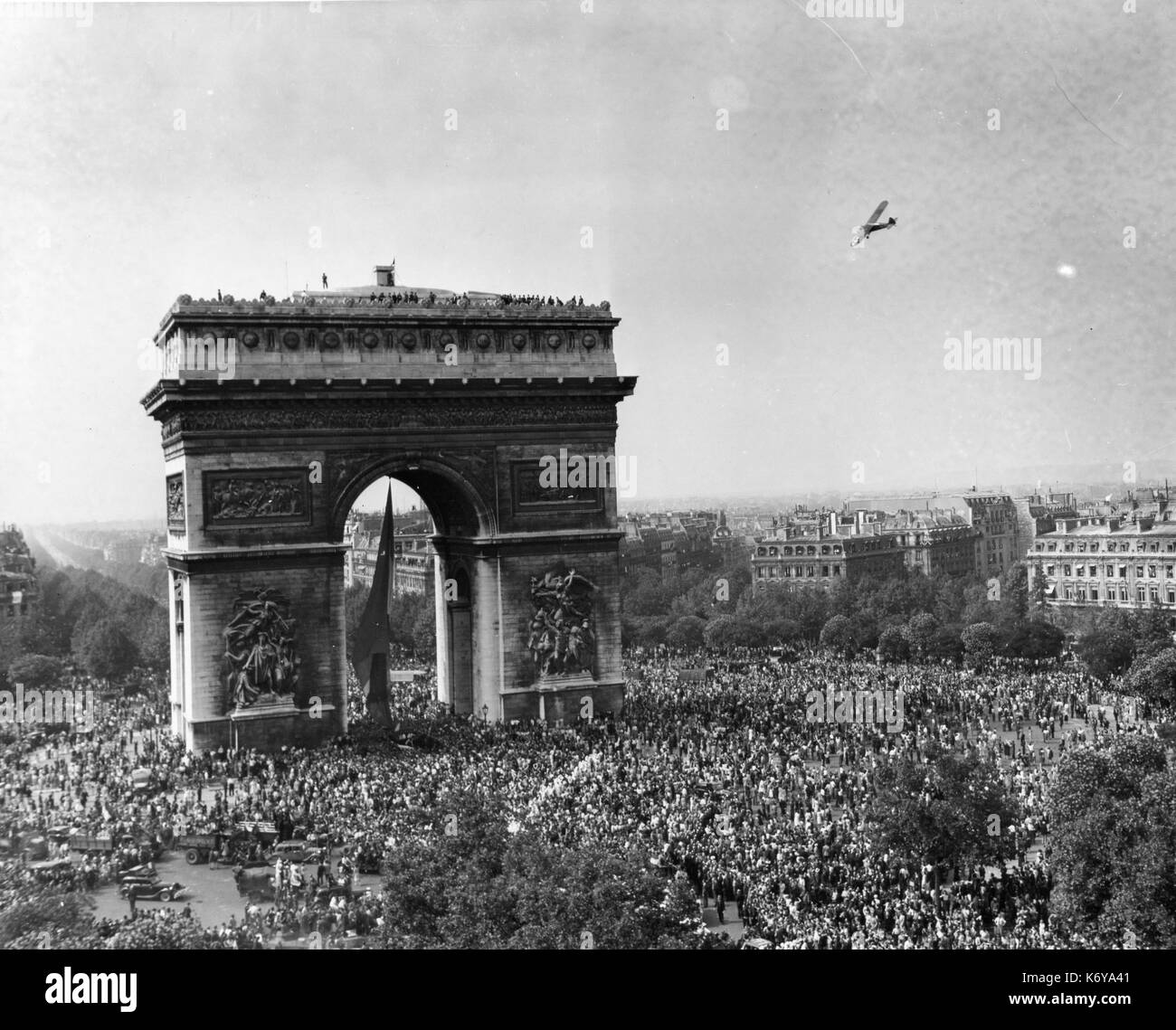 Parisians mass around the Arc de Triomphe as a circling plane dips in salute to the men of the Allied armies who liberated the city. All Paris turned out to greet French and US units as they entered the city in triumph. Paris, France, 8/26/44. Stock Photo
