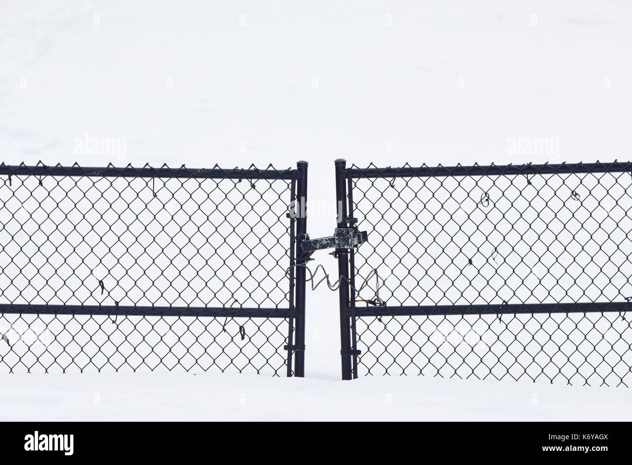 Closed and locked chain link fence gate on a snowy driveway in