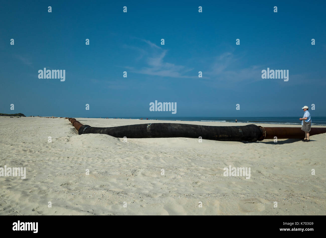 Am Strand, Langeoog.  Deutschland.  Germany.  A tourist inspects the commercial pipeline used as part of the active beach rebuilding, Strandaufschüttung.  It's the scale of the pipeline and breadth of the sandy beach become apparent. Stock Photo