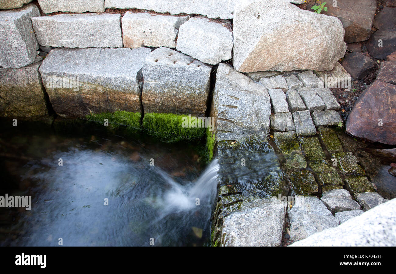 a flowing small waterfall beside green algae growing on white stones Stock Photo