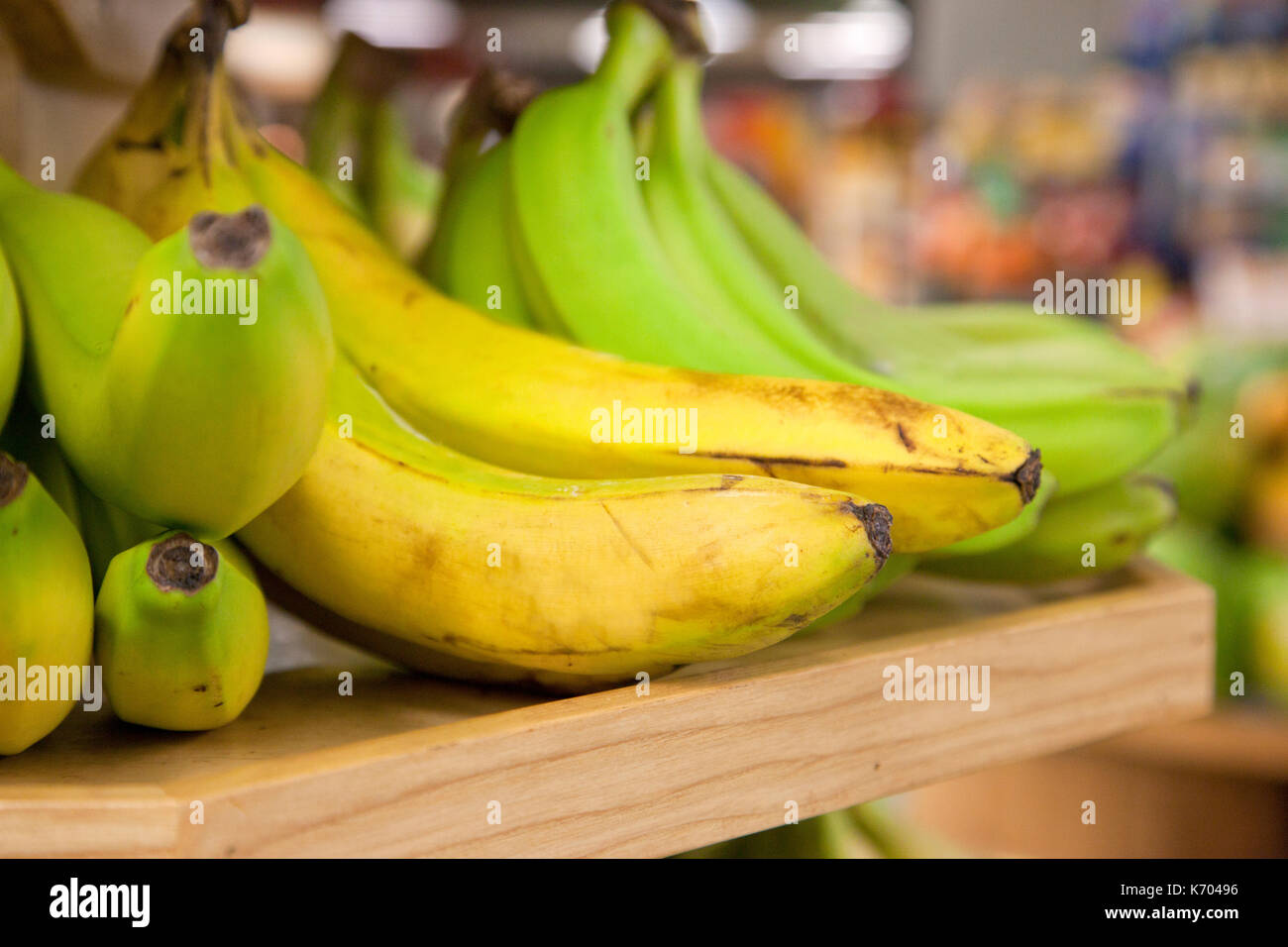 bunches of imperfect yellow and green bananas, in a store on a shelf Stock Photo