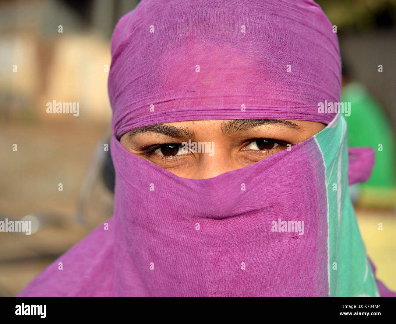 Young Indian woman with scrutinizing eyes covers her hair and face with a trendy secular headscarf and poses for the camera. Stock Photo