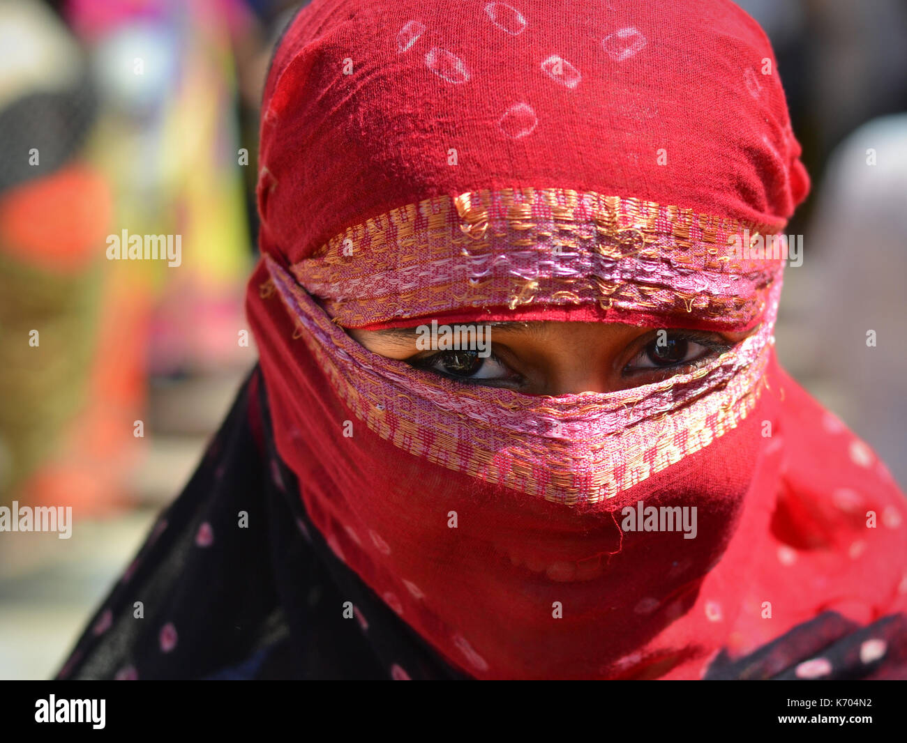 Young Indian woman with smiling eyes coverd her hair and face with a trendy half-sheer head scarf in red. Stock Photo