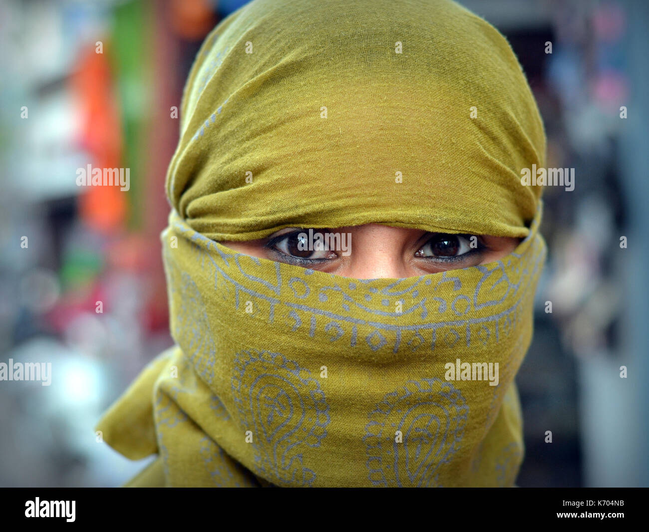 Young Indian woman with beautiful eyes covers her hair and face with a trendy secular, yellow headscarf and poses for the camera. Stock Photo