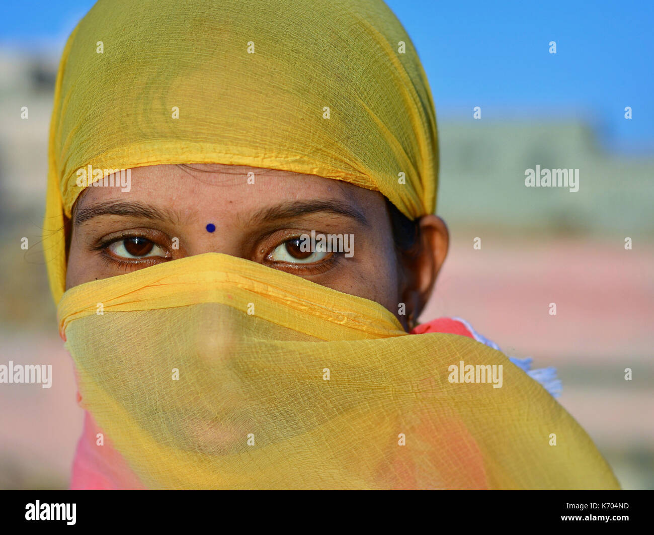 Young Indian woman covers her hair and face with a trendy secular, half-sheer yellow headscarf and poses for the camera. Stock Photo