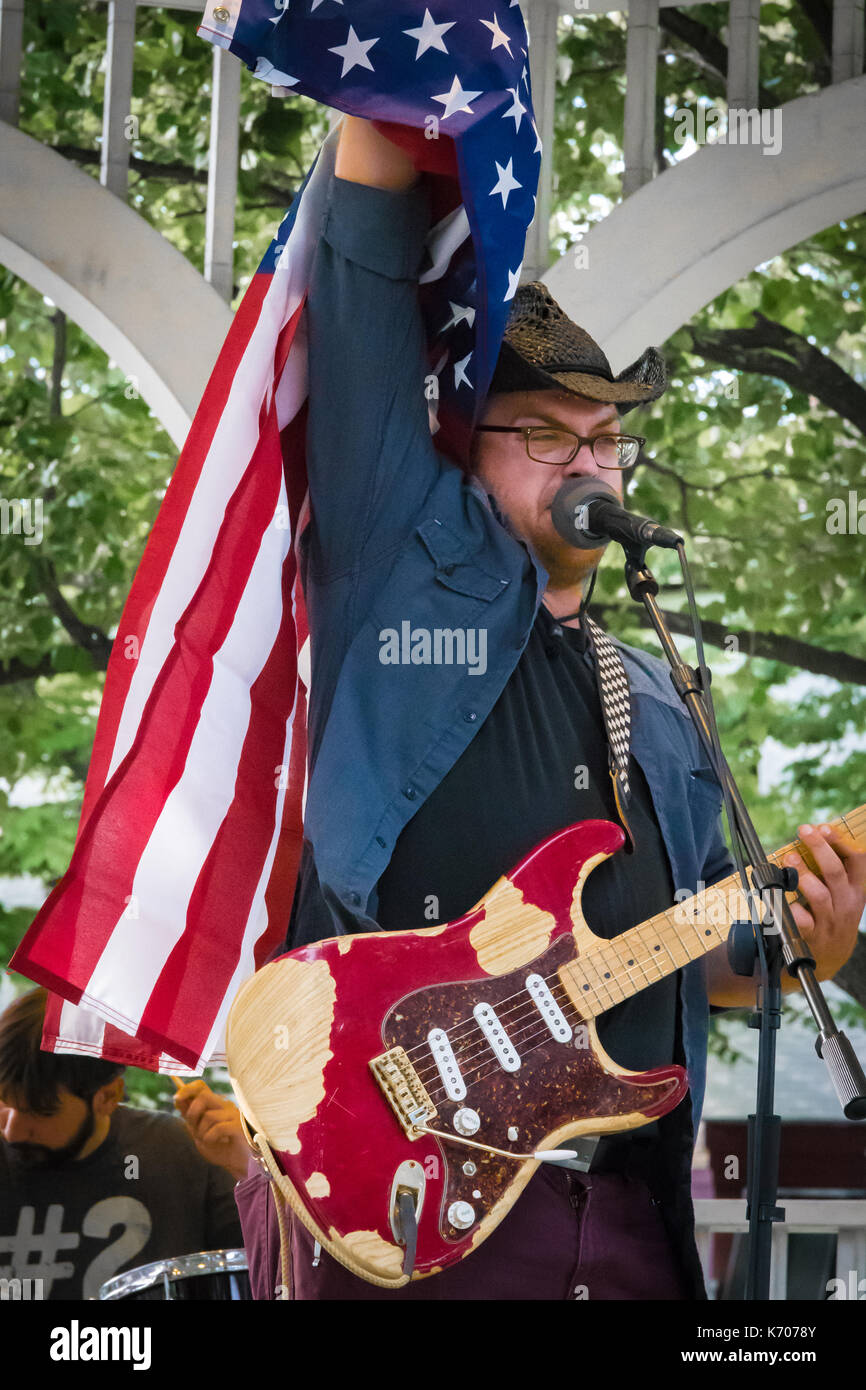 A Caucasian male singer raises an American flag during an outdoor local music festival. Stock Photo