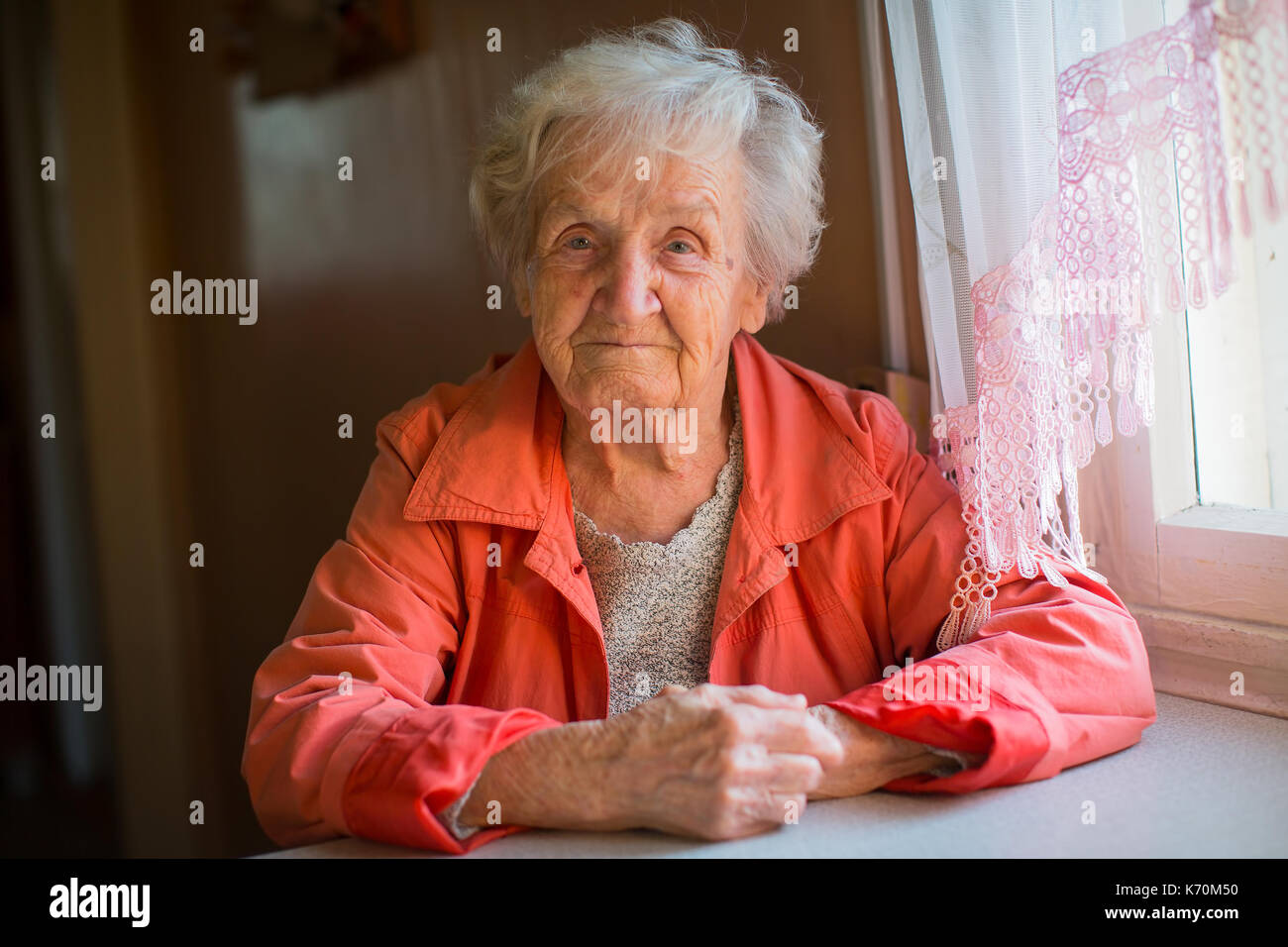 Elderly woman in red jacket sitting at table portrait. Stock Photo