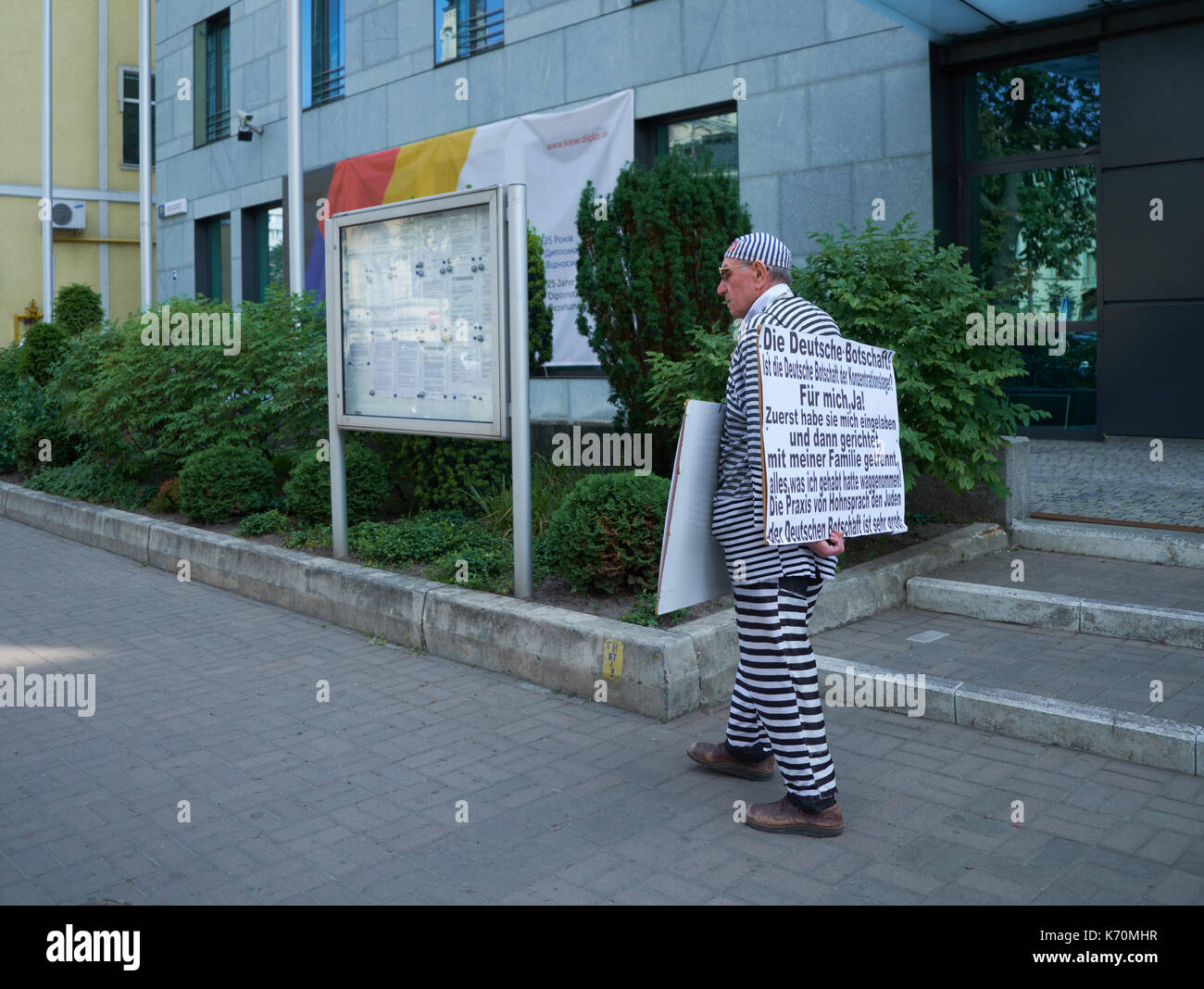 Kyiv, Ukraine - June 06, 2017: Old man in prisoner costume carries poster with blaming to the German embassy in front of German embassy building in Ky Stock Photo