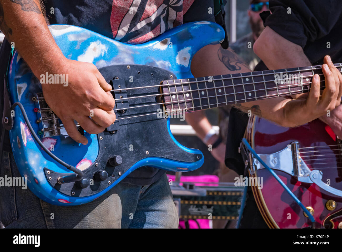 A blue bass guitar being played at a local outdoor rock concert. Stock Photo