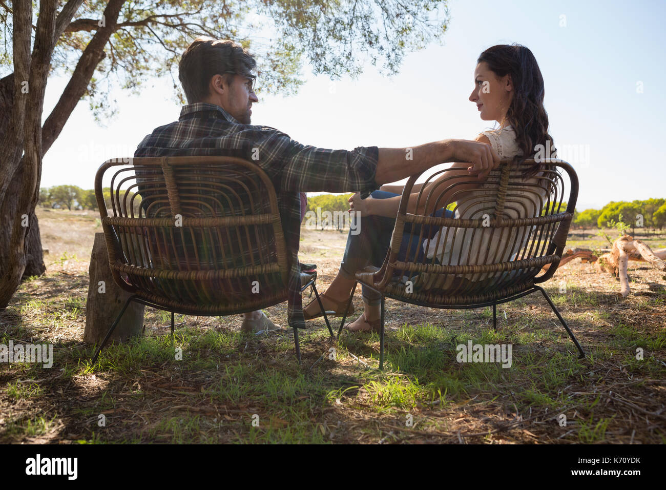 Young couple looking each other while sitting on chairs at field Stock Photo