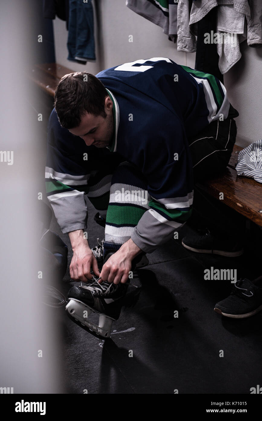 Male ice hockey player tying skate while sitting in dressing room Stock Photo Alamy