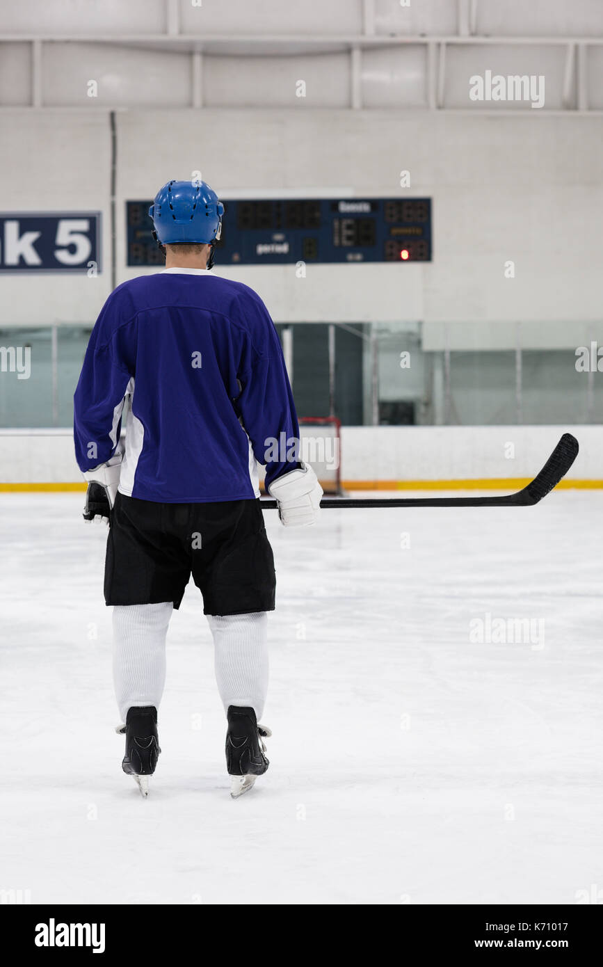 Rear view full length of male player holding ice hockey stick at rink