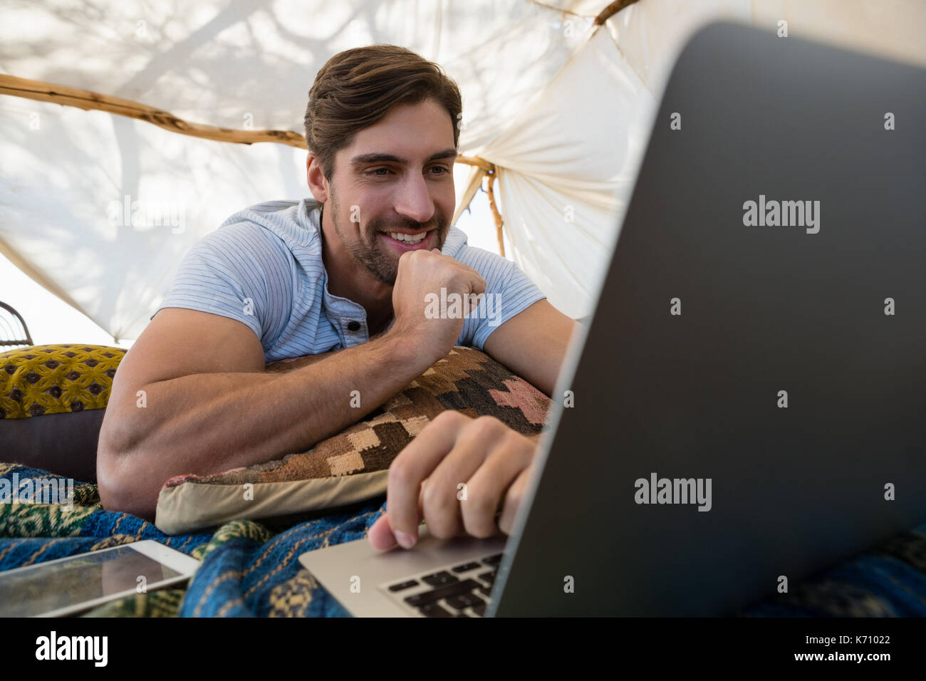 Smiling young man using laptop while lying down in tent Stock Photo