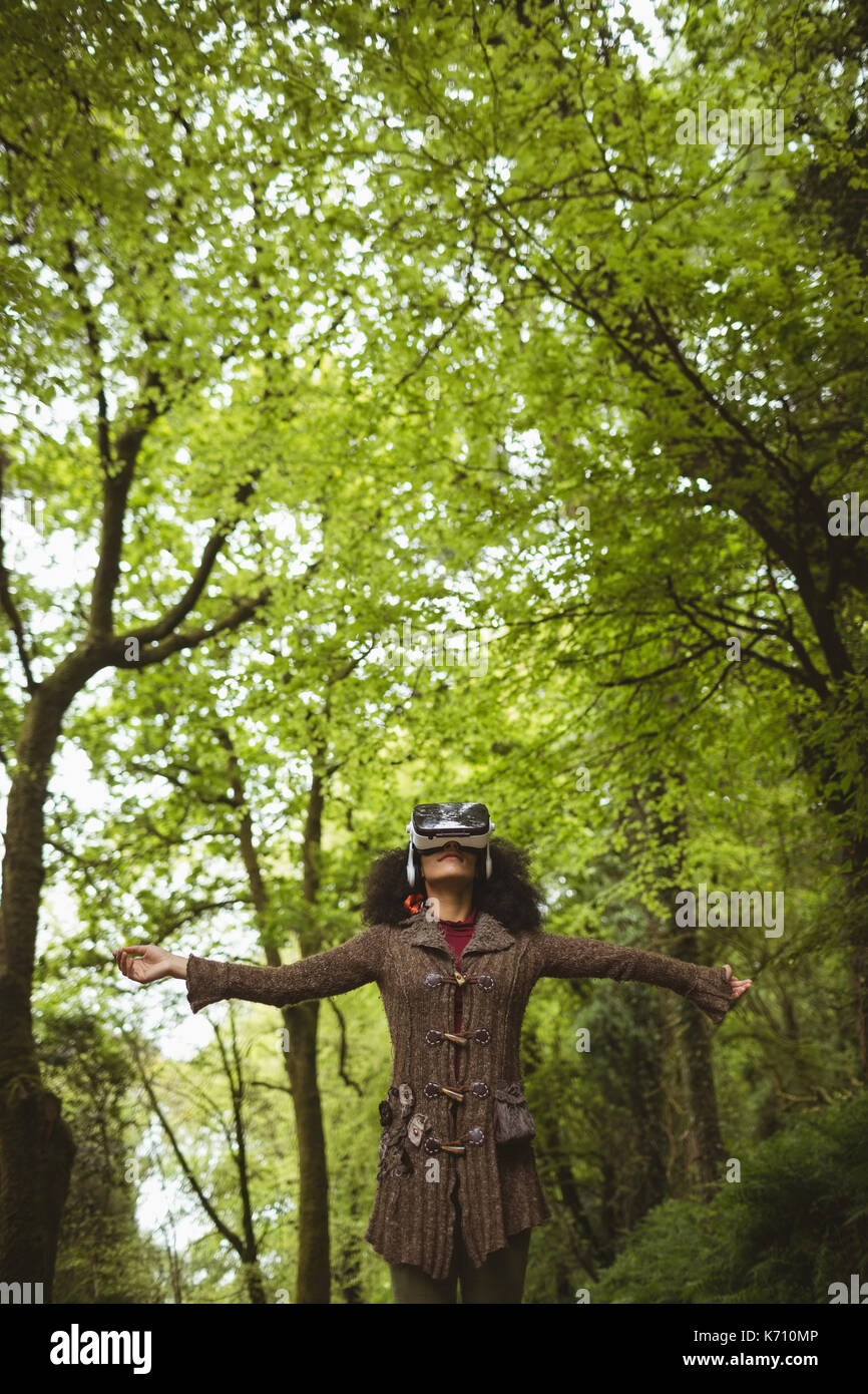 Woman with arms outstretched wearing virtual reality headset at forest Stock Photo