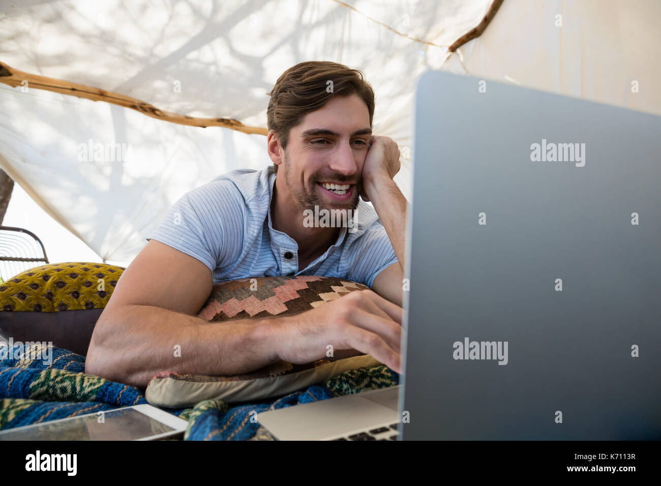 Happy young man using laptop while lying down in tent Stock Photo