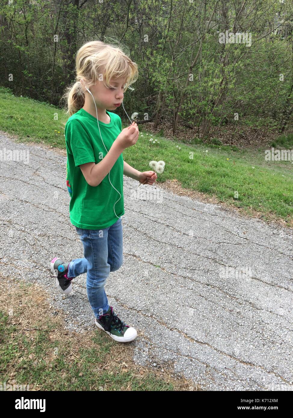 Little girl blowing dandelion while on a walk and listening to music Stock Photo