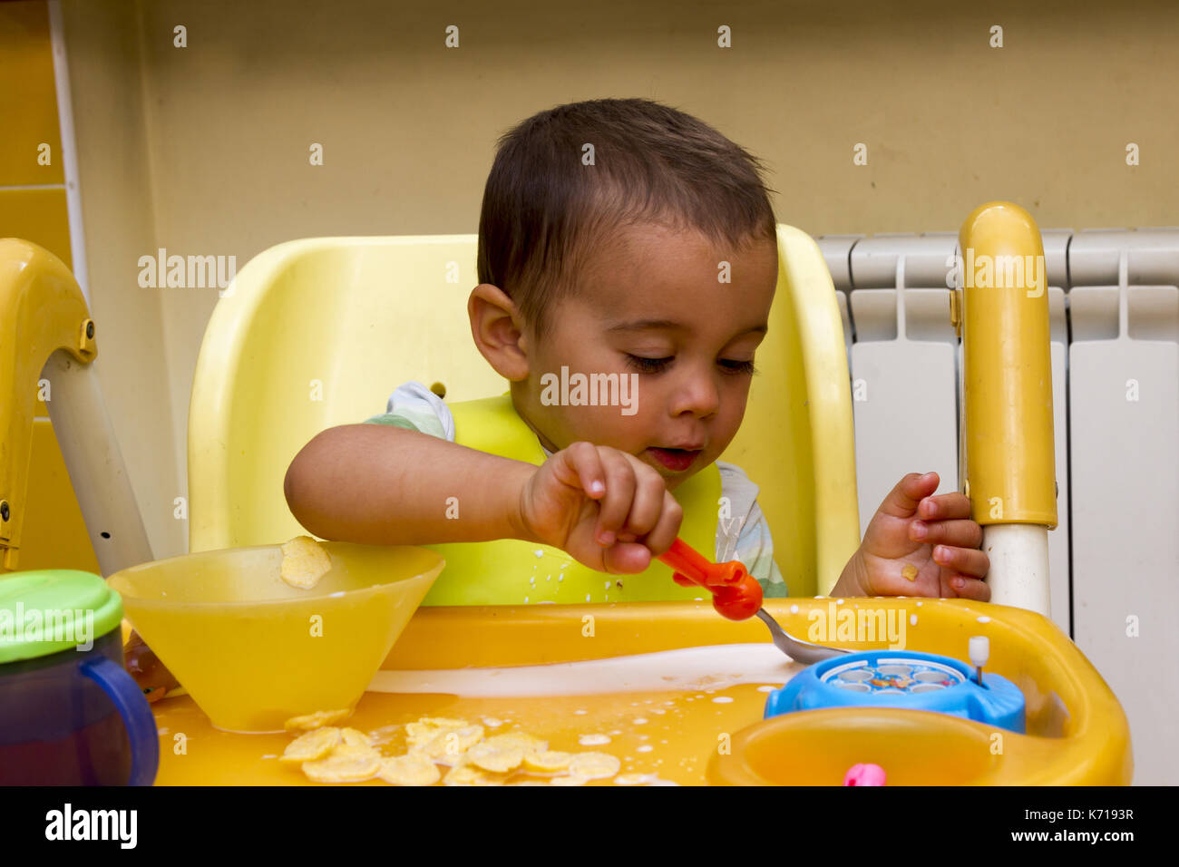 A little boy is sitting in a child's chair and eating Stock Photo