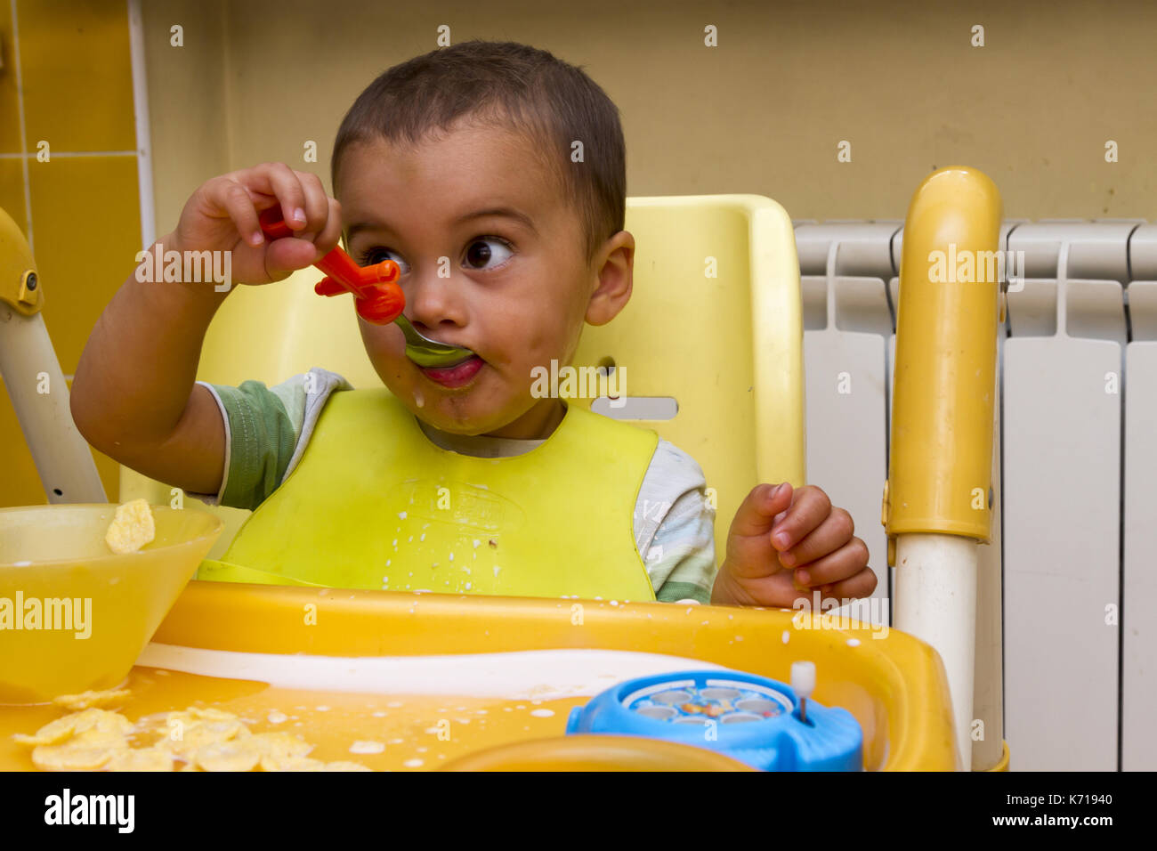 A little boy is sitting in a child's chair and eating Stock Photo