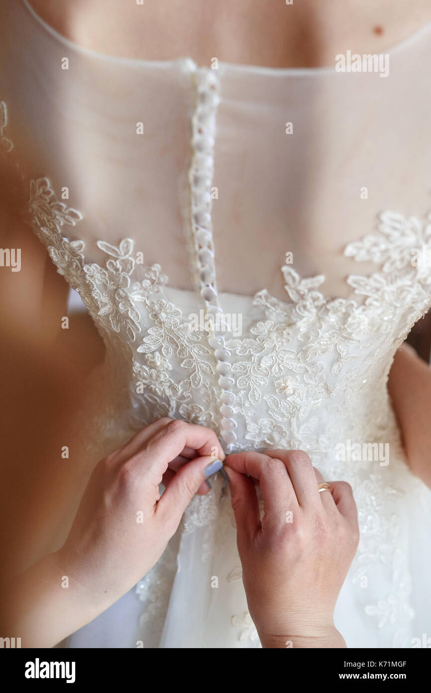 bridesmaid helps dress the bride to white wedding dress Stock Photo
