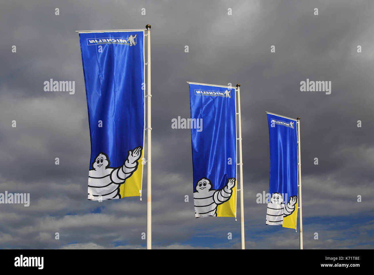Company flags with logo Bibendum figure flying dark cloud sky, Michelin factory and research establishment, Almeria, Spain Stock Photo