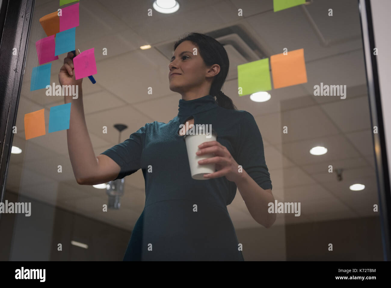 Businesswoman writing on sticky note seen through glass in office Stock ...