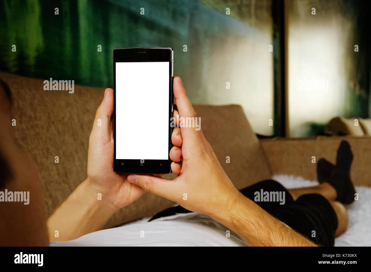 Man relaxing during looking at the screen while lying on sofa - blank screen smartphone Stock Photo