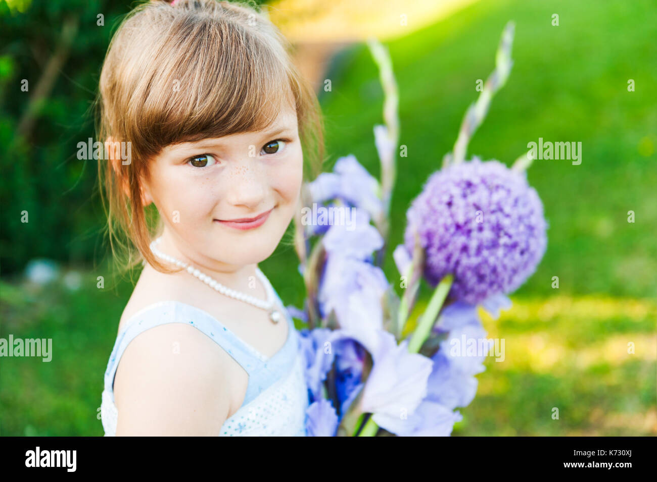 Outdoor portrait of a cute little girl with beautiful bouquet of purple ...