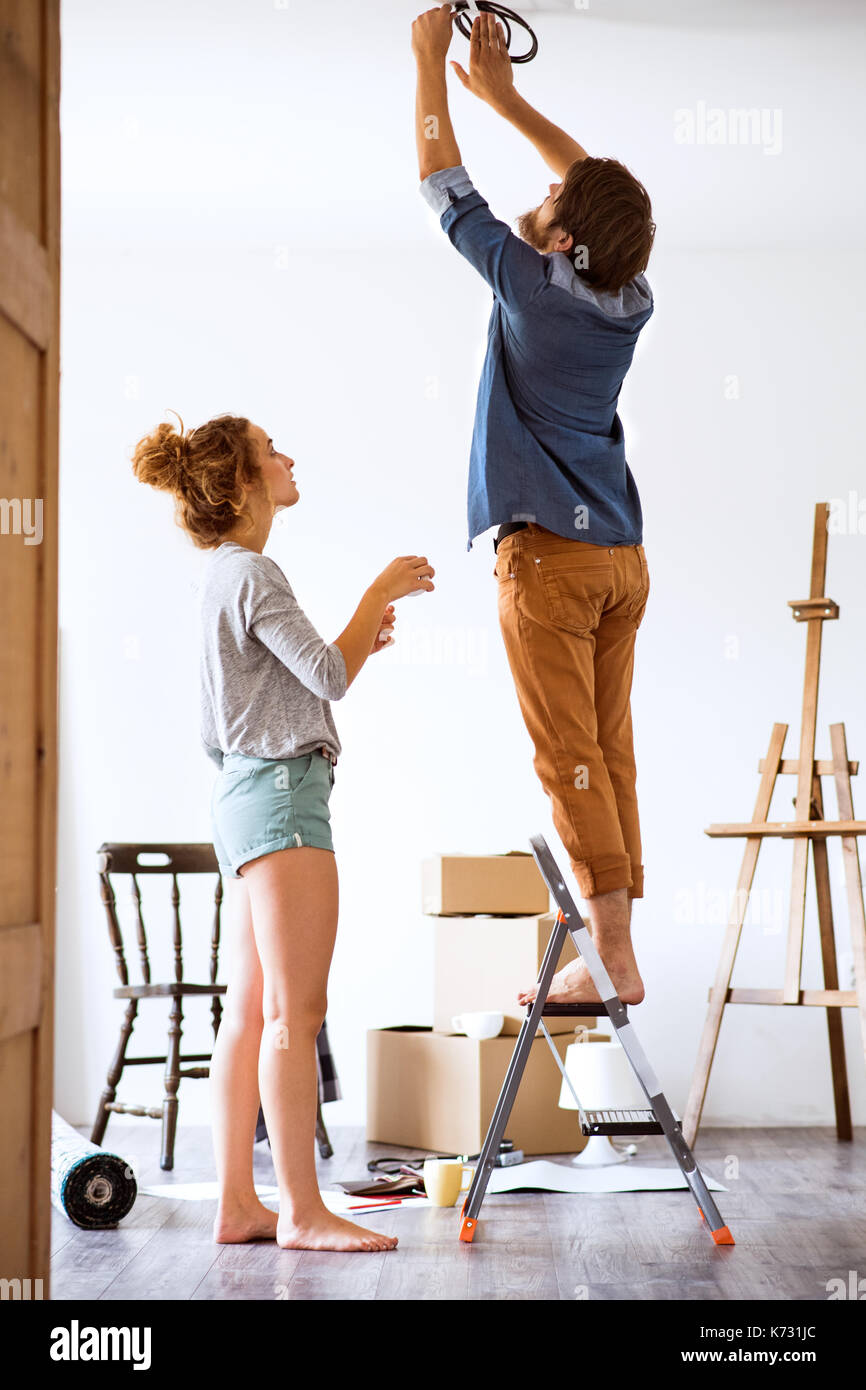 Young couple moving in new house, changing a light bulb. Stock Photo