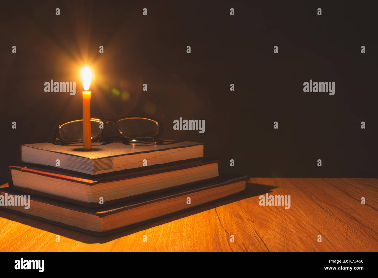Close-up of burning candle with pile of old book on wooden table. Education concept. Stock Photo