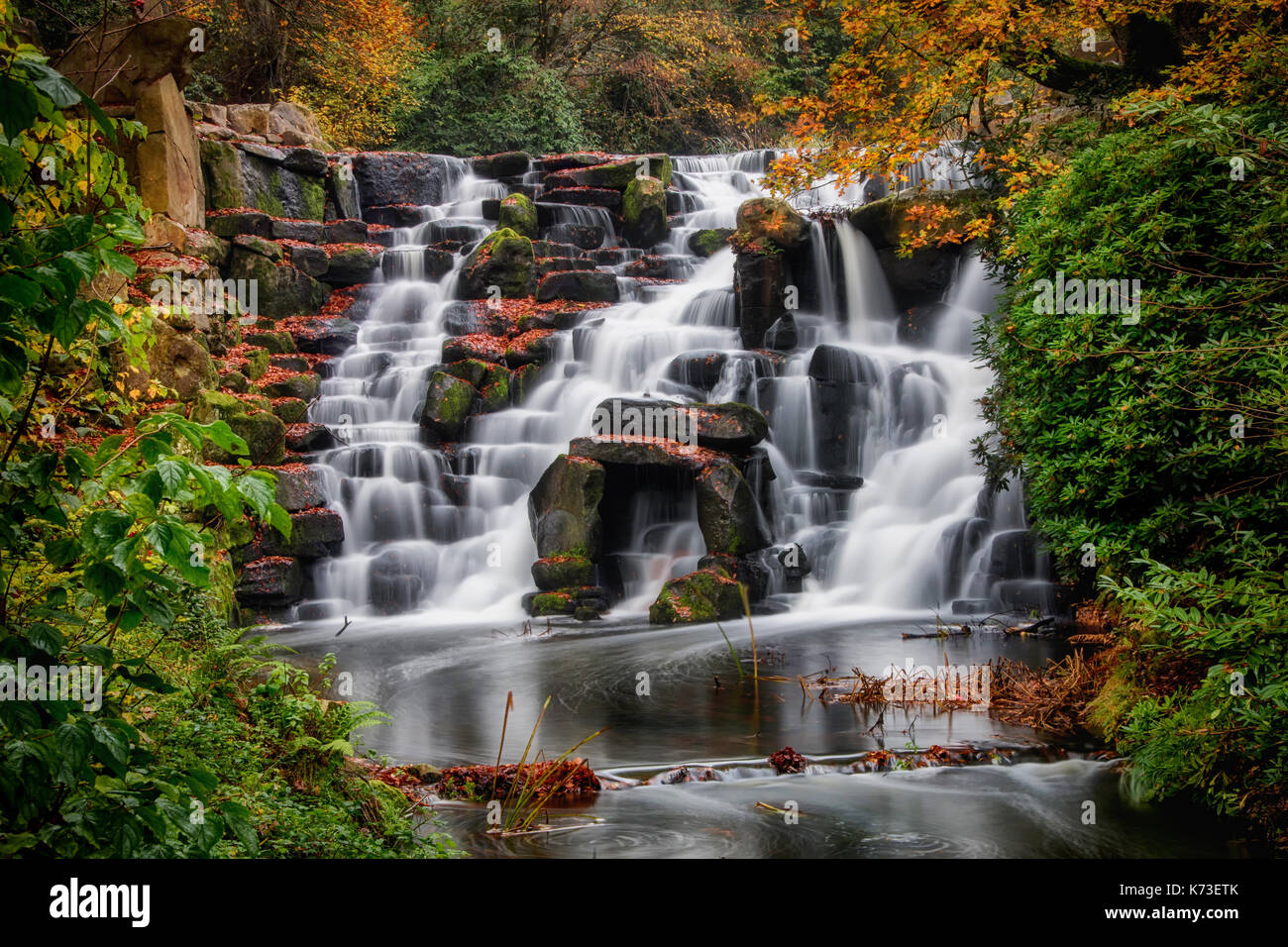 The Cascades Waterfall in Autumn. Virginia Water, Surrey. UK.  A long exposure gives the milky white motion blur of water rushing over the rocks Stock Photo