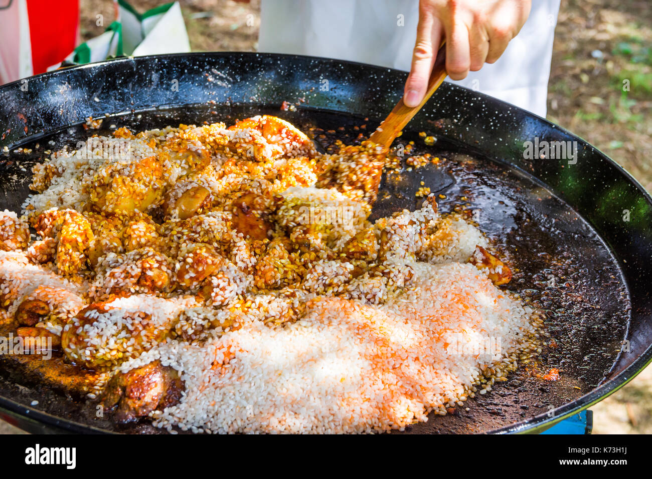 Man's hand holding wooden turner, mixing uncooked rice with fried ...