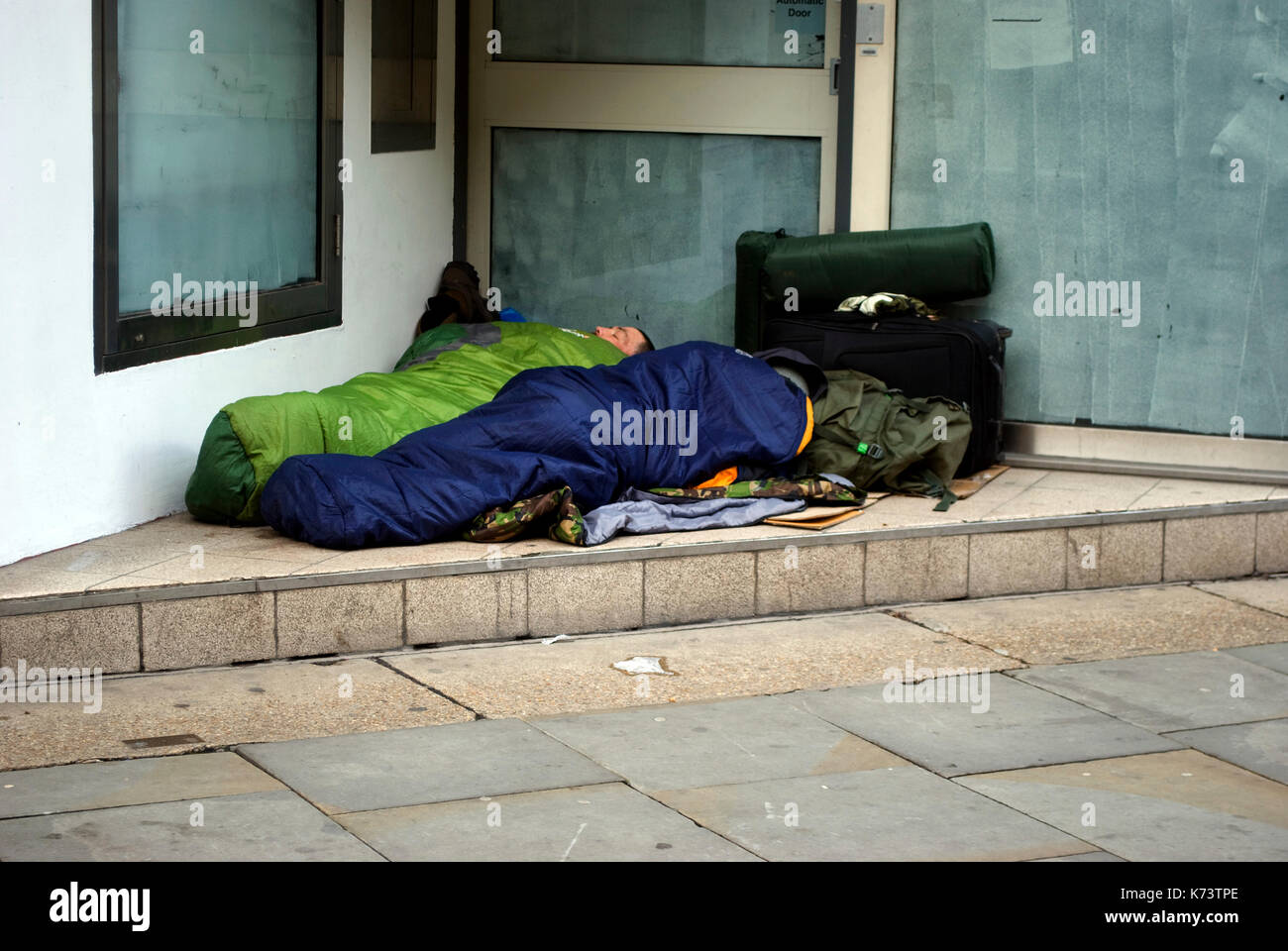 Two homeless people seeking shelter in a doorway, Manchester UK Stock