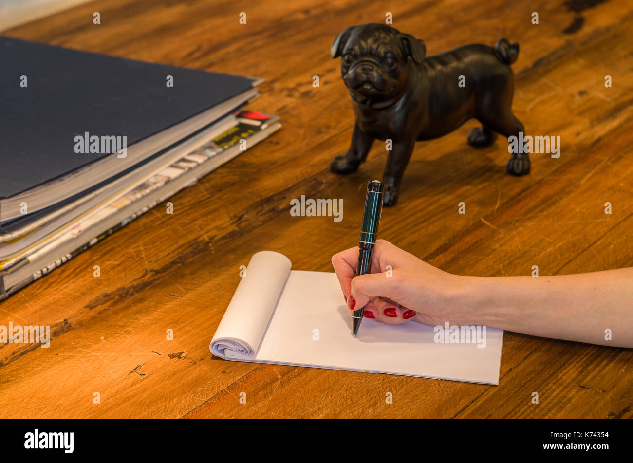 Woman hand writing on blank notepad on top of rustic wooden table with  decorative objects, pug sculpture Stock Photo - Alamy