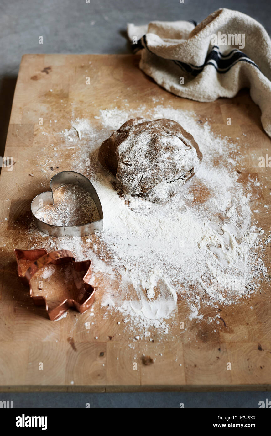 Kitchen photo of a dusted wooden chopping board and antiqued t-towel with uncooked, prepared, cookie dough cut into festive shapes for Christmas. Stock Photo