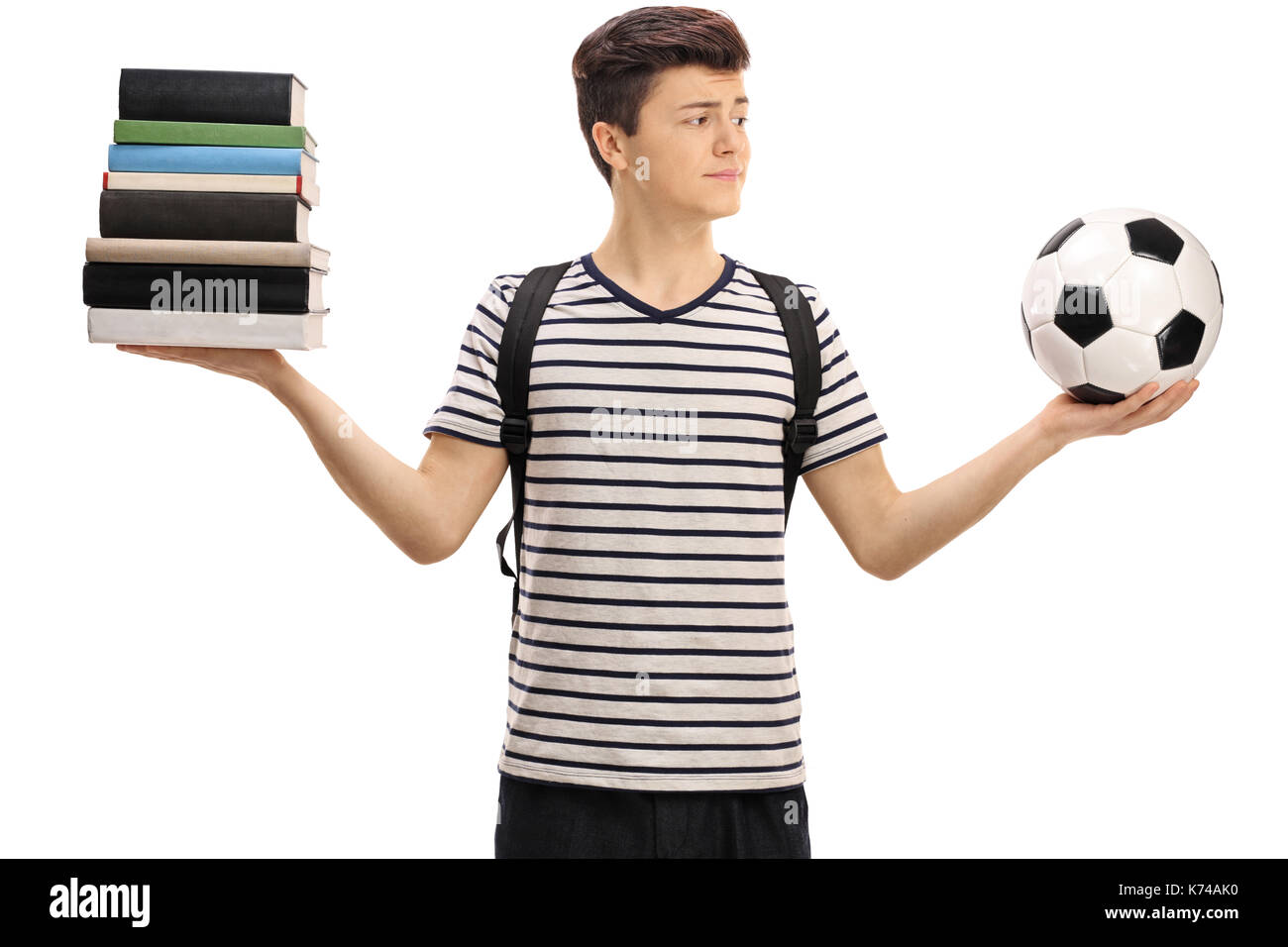 Indecisive teenage student holding a football and a stack of books isolated on white background Stock Photo