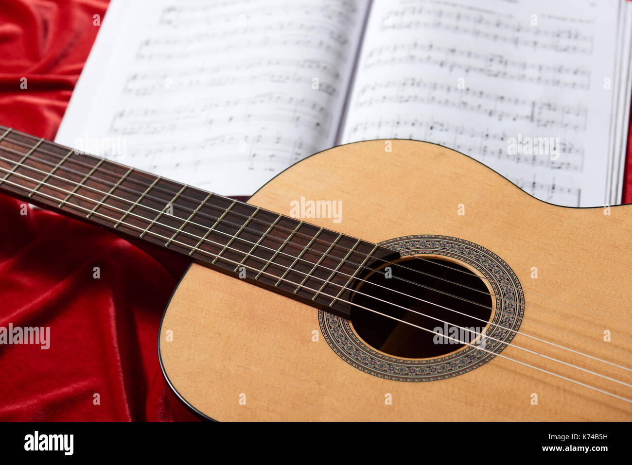 acoustic guitar and music notes on red fabric, close view of objects ...