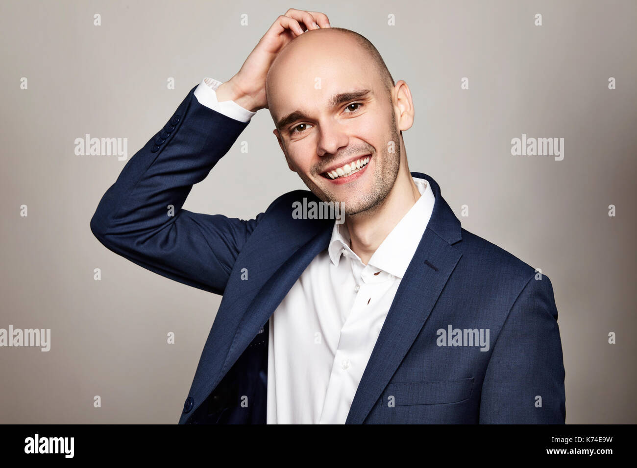 Close-up portrait of a young bald man stroking his head. He is smiling. Gray background. Horizontal. Stock Photo